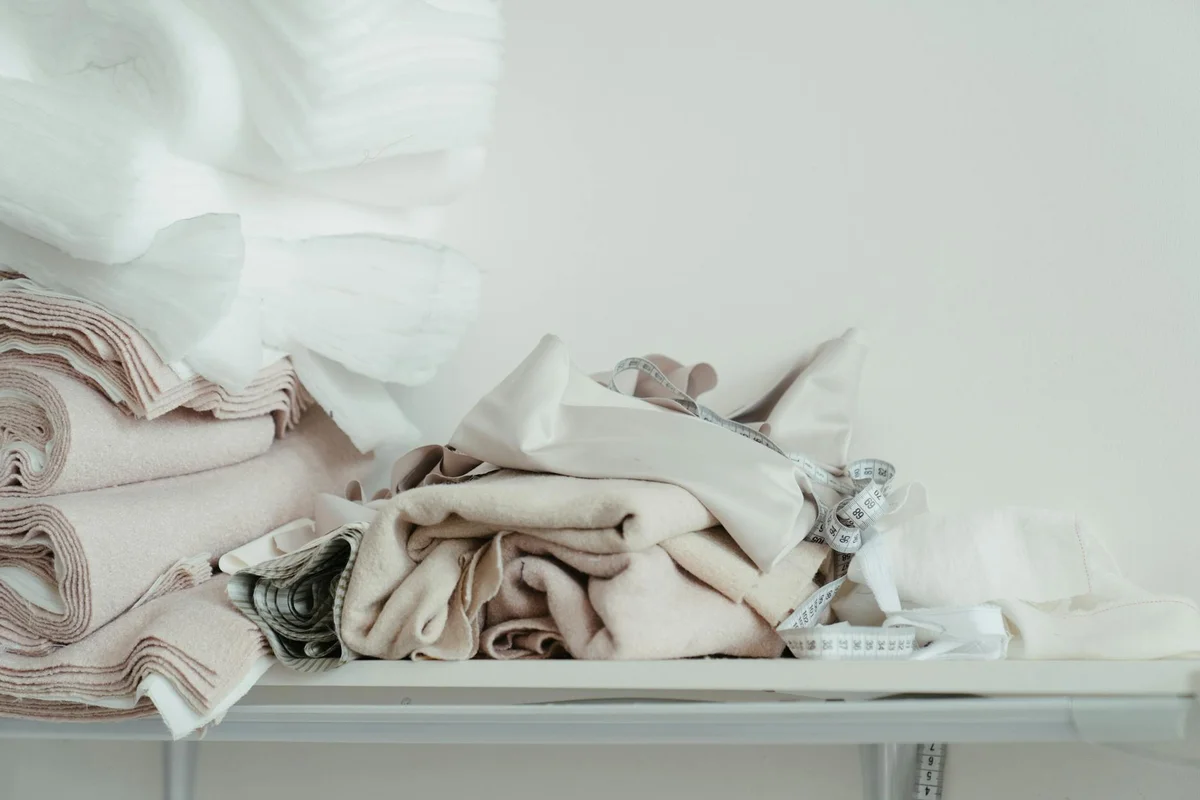 Flat lay of folded beige and white fabrics on a shelf with a measuring tape