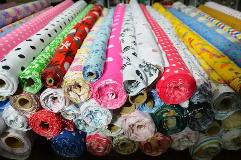 A pile of colorful rolled fabrics with various patterns laid out in a shop.