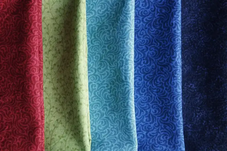 Rows of colorful patterned fabrics with ornate swirl designs in red, green, teal, blue, and navy.