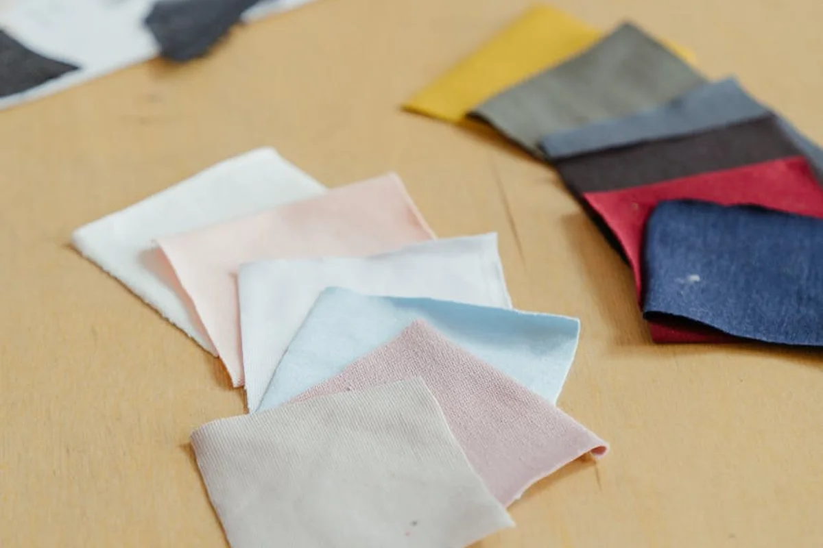 Assorted fabric swatches in pastel and earthy tones laid out on a wooden surface, representing fabrics to compare in water, weather, and wear tests.