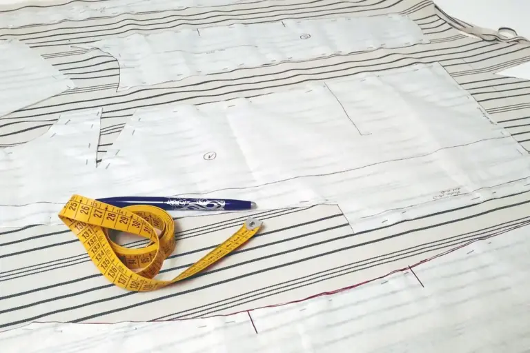 Measuring tape on fabric with pattern pieces and a pen, illustrating yardage conversion for sewing projects