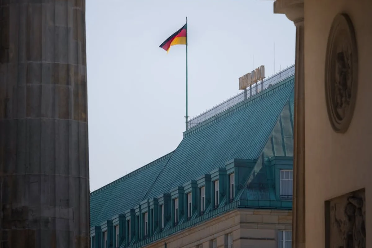 Flag atop a historic building with a green roof, framed by stone columns and a doorway arch.