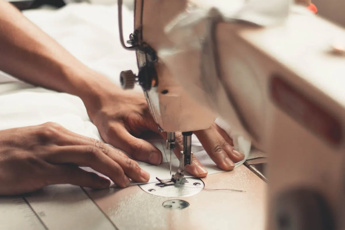 Close-up of hands guiding fabric through a sewing machine, illustrating the making of gabardine fabric in tailoring.