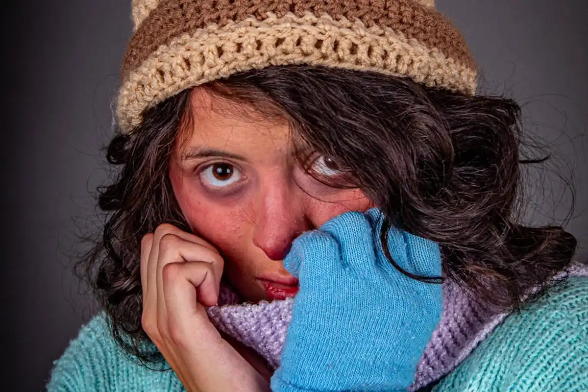 Close-up of a person wearing a knit hat and a colorful sweater, looking at the camera with a thoughtful expression.