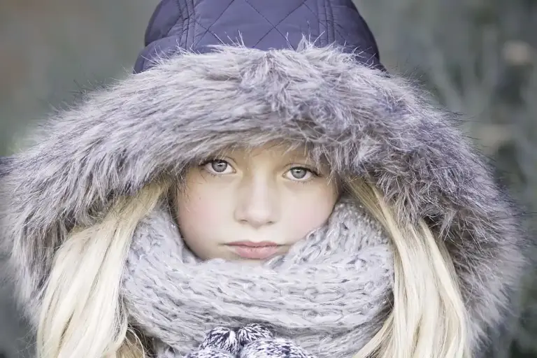 Young girl wearing a gray faux fur-lined hood and scarf in winter.