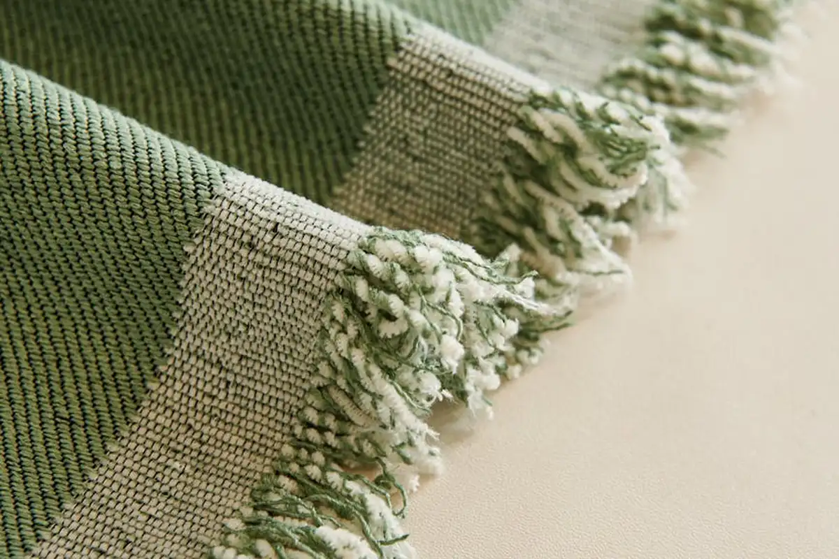 Close-up of green woven fabric with fringed edge resting on a light surface