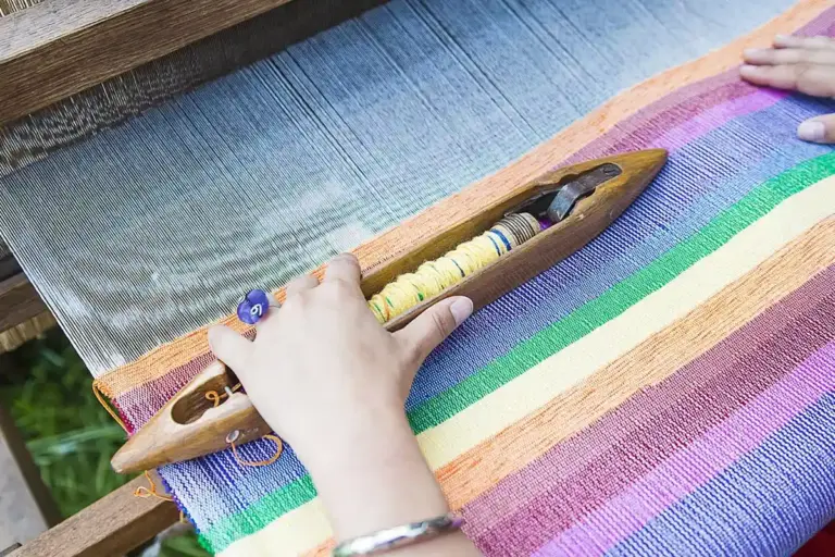 Hands weaving colorful striped cotton fabric on a loom
