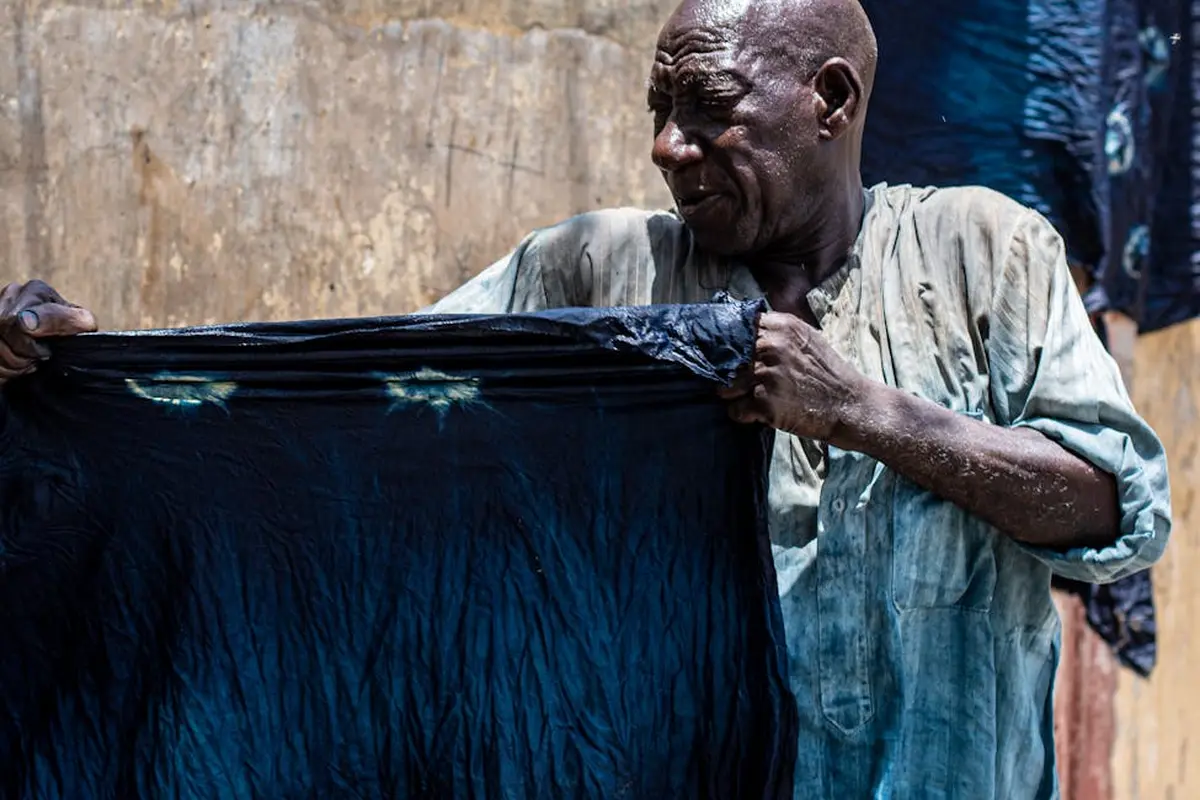 A person holds a large, dark fabric outdoors, likely during a home dyeing process.
