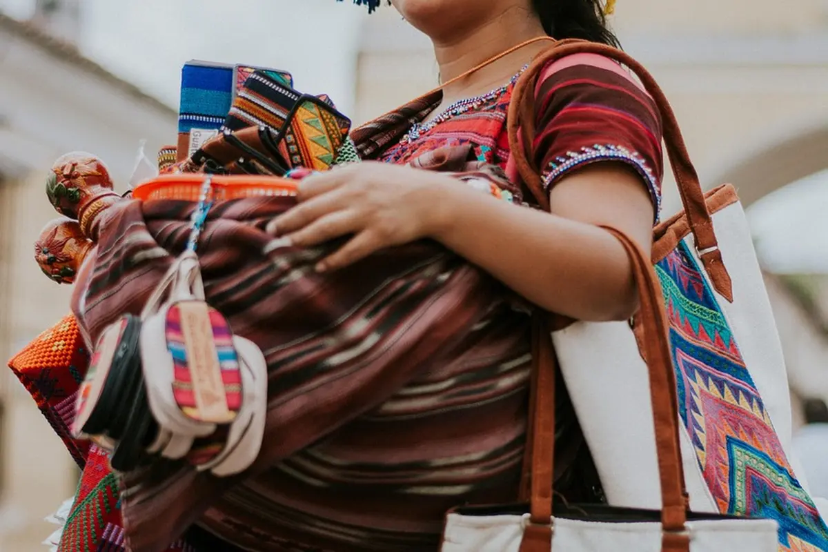 Person wearing a patterned red top carrying multiple colorful shopping bags.