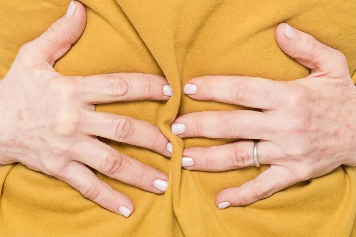 Close-up of hands pinching mustard-yellow fabric, showing folds and tension, to illustrate caution before bleaching polyester-spandex or nylon fabrics.