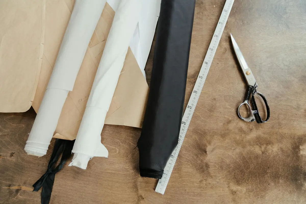 Assorted fabric swatches in white and black on a wooden worktable with a measuring tape and scissors