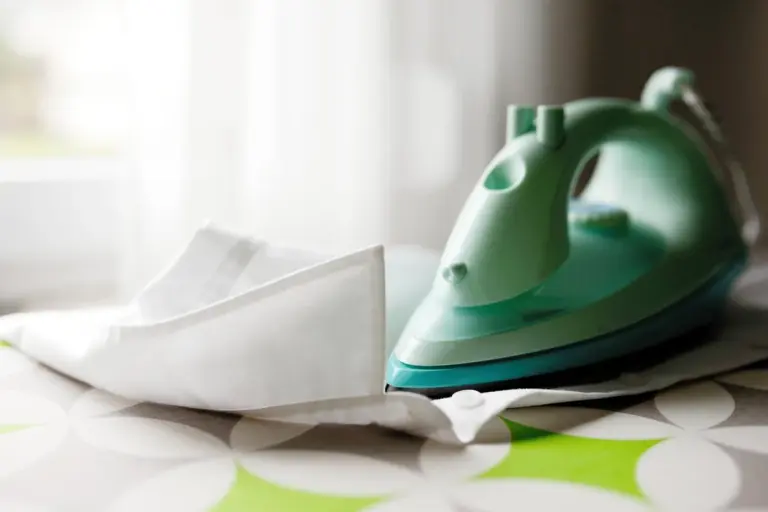 Teal electric iron resting on a white fabric, prepared for pressing delicate materials.