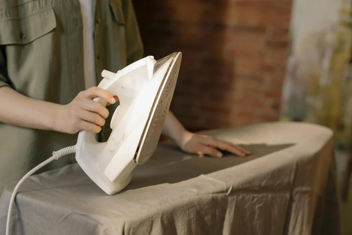 Person ironing a garment on an ironing board with a white steam iron