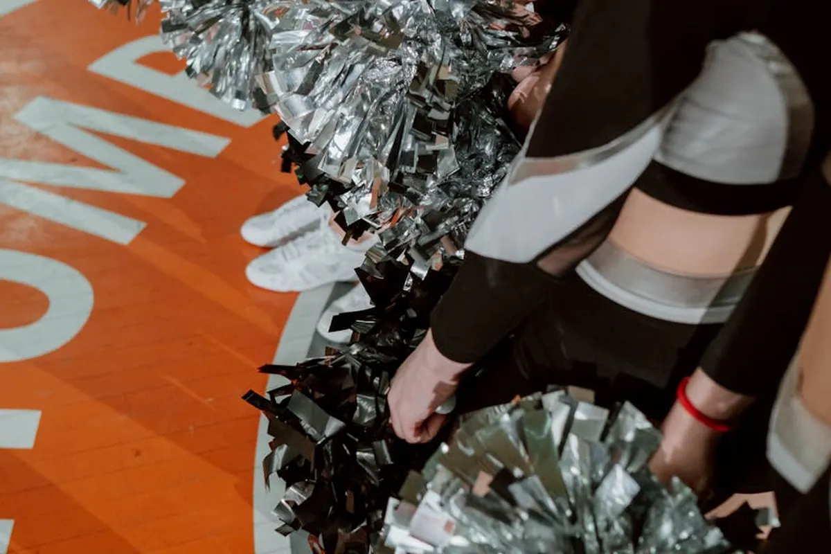 Person in black and white athletic wear with metallic silver pom-poms on an orange floor