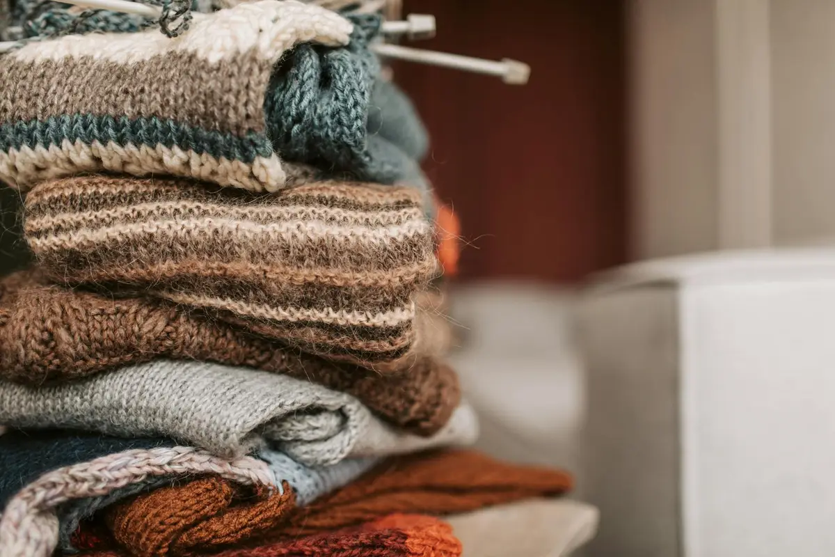 Stack of folded knitted sweaters in earthy browns and creams, showing varying knit textures and fabric layers