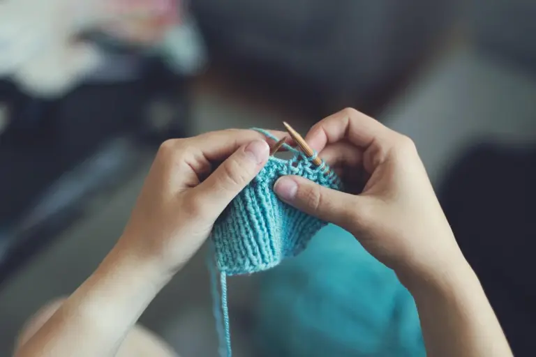 Close-up of hands knitting with turquoise yarn and knitting needles