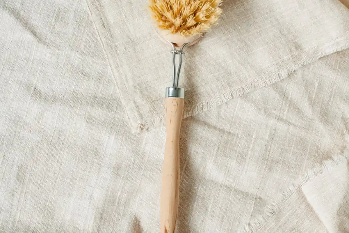 Close-up of a wooden-handled fabric brush resting on light linen fabric.