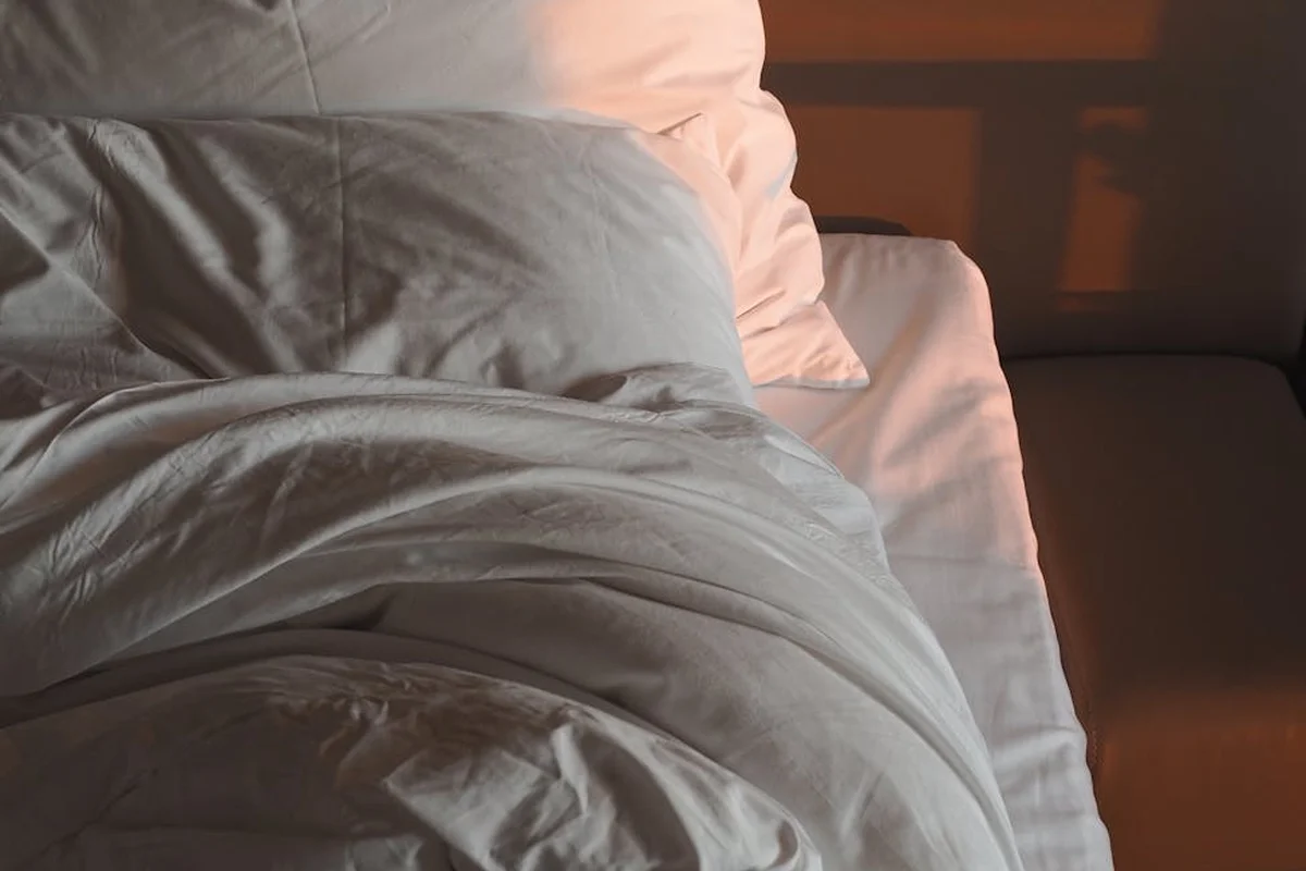 Close-up of rumpled white bed linens and pillows on a softly lit bed.