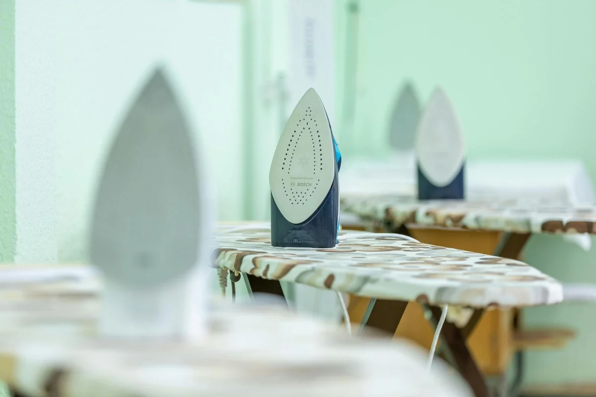 Row of irons on ironing boards in a bright laundry area, illustrating the ironing step of care for linen and cotton fabrics.