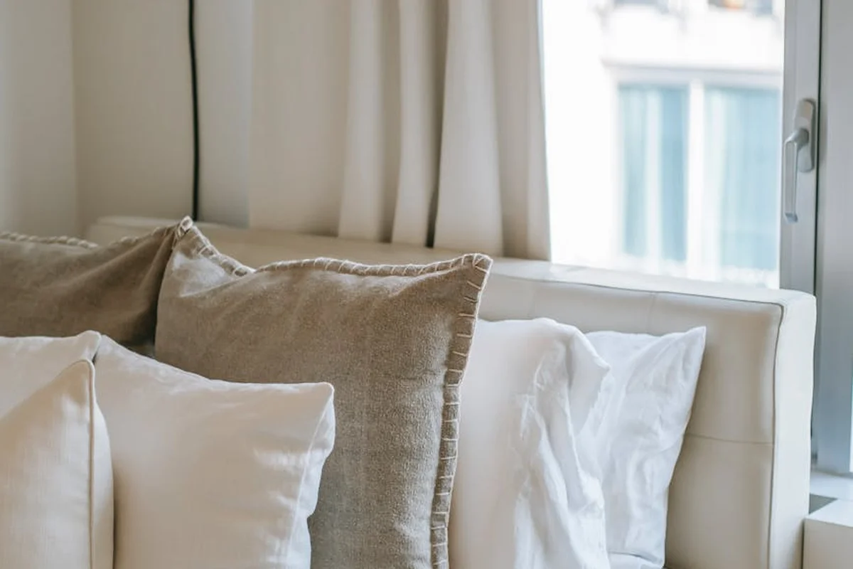 Close-up of beige and white linen cushions on a sofa beside a window, highlighting natural texture and soft drape.
