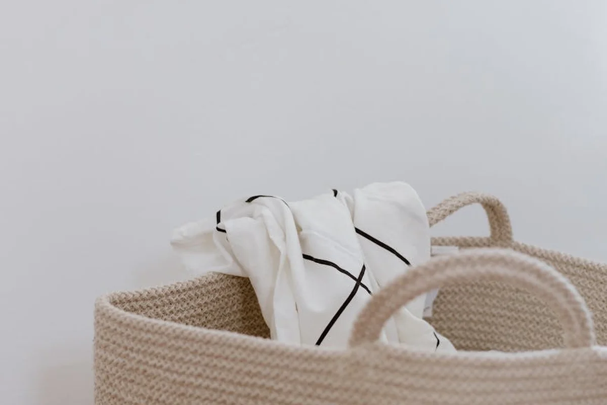 Beige woven laundry basket with a white cloth draped over the edge against a neutral wall.