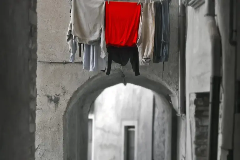 Clothesline strung across a narrow archway with garments hanging to dry, featuring a striking red piece among neutral-colored fabrics.