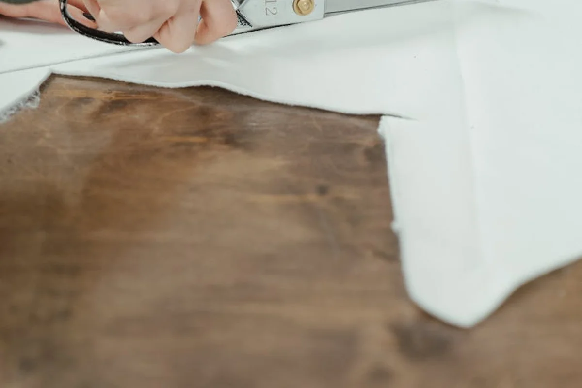 Close-up of hands using scissors on fabric on a white surface, with a brown patch, illustrating careful handling to prevent damage to linen and velvet.