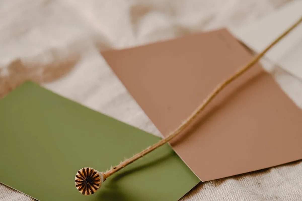 Close-up of fabric swatches in green and brown with a wooden thread spool lying nearby