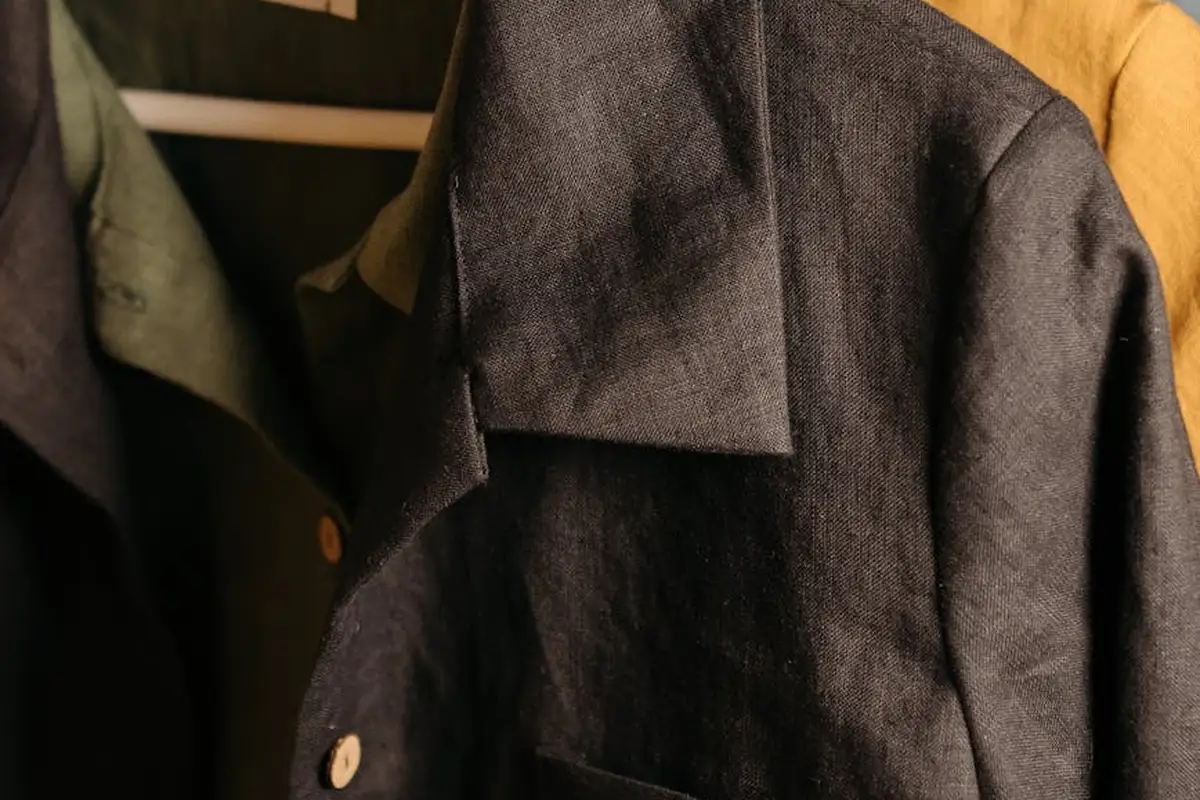 Close-up of dark linen-like fabric on a garment, revealing the weave, collar, and buttons.