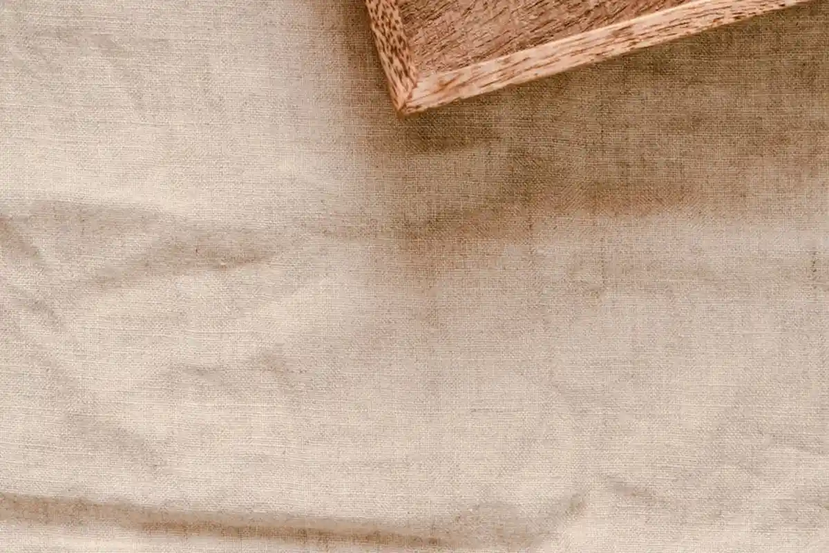 Close-up of wrinkled beige linen fabric with a small woven wooden block in the top-right corner