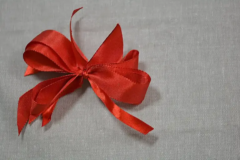 Red ribbon tied into a bow on light gray linen fabric
