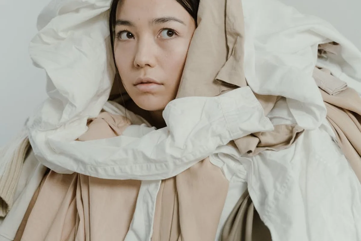 Person wrapped in layered beige and white fabrics, embodying texture, comfort, and luxury