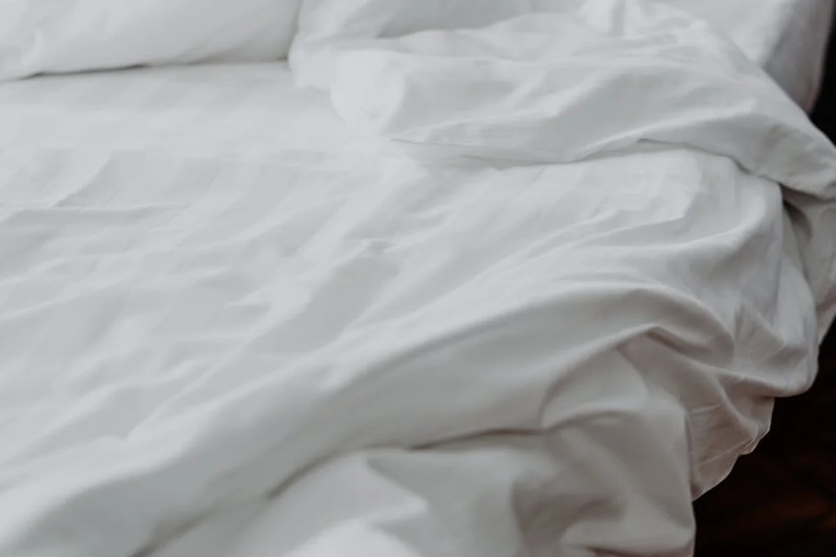 Close-up of white linen fabric with soft wrinkles, highlighting natural texture and subtle shade variations.