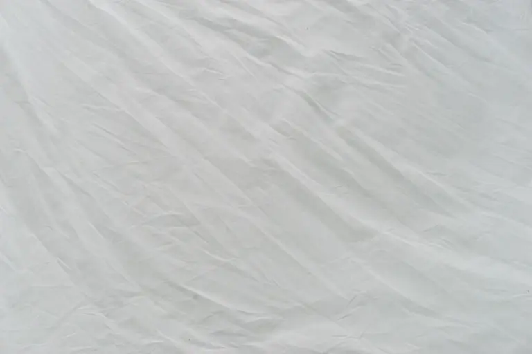 Wrinkled white linen fabric laid flat, showing texture and the care steps needed to prevent shrinkage while washing, drying, and ironing.