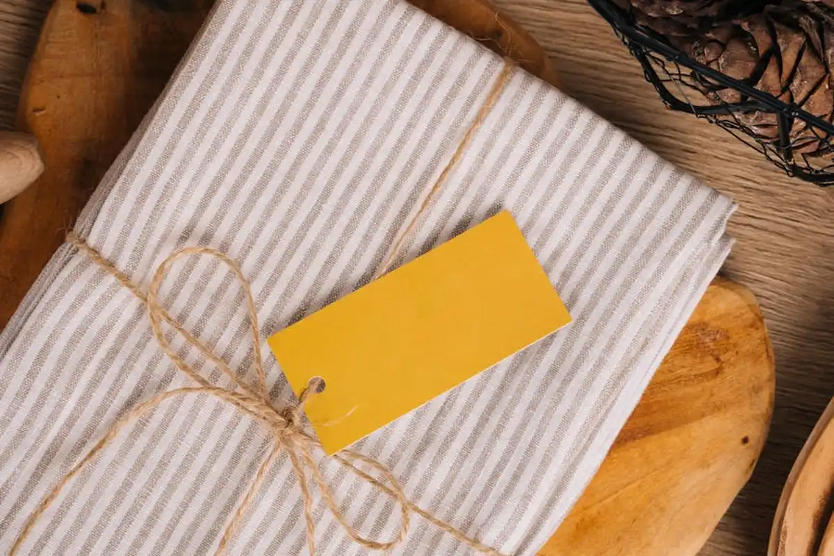 Wrapped linen fabric with light gray stripes tied with twine and a yellow gift tag on a wooden surface