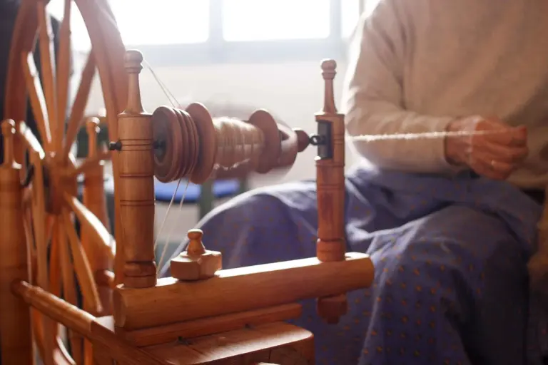 A person weaving on a wooden loom, with warp threads and spools visible, illustrating fabric construction that affects UV protection.