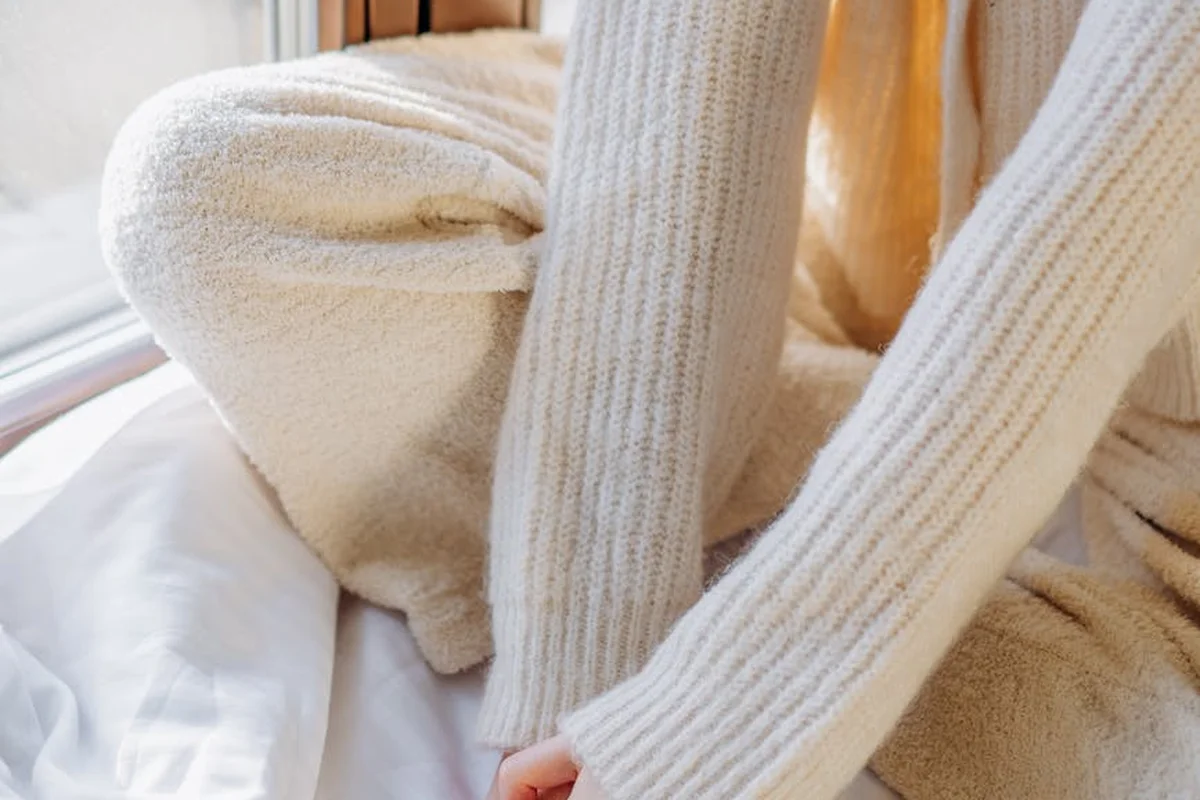 Cozy cream knit sweater and blanket draped near a sunlit window, illustrating fabric care and comfort.