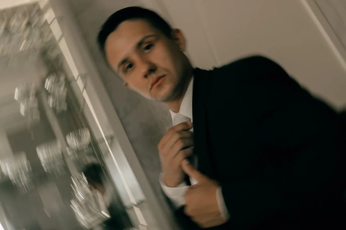 A man in a dark tailored suit adjusts his tie in an indoor setting, conveying formal linen-suit styling.