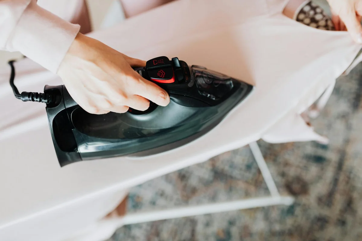 A hand holds a steam iron gliding over fabric on an ironing board, illustrating the ironing step of modal cotton care.