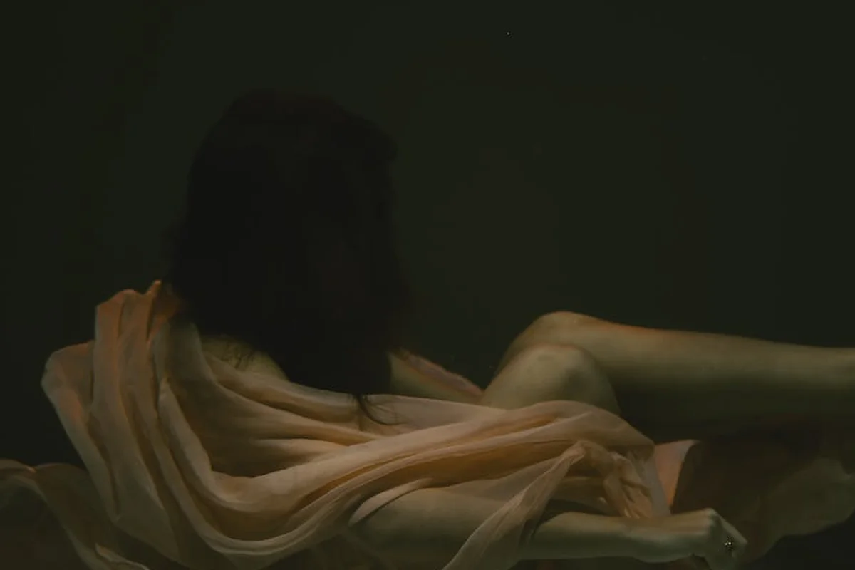 Soft peach fabric draped over a reclining figure in dim lighting.