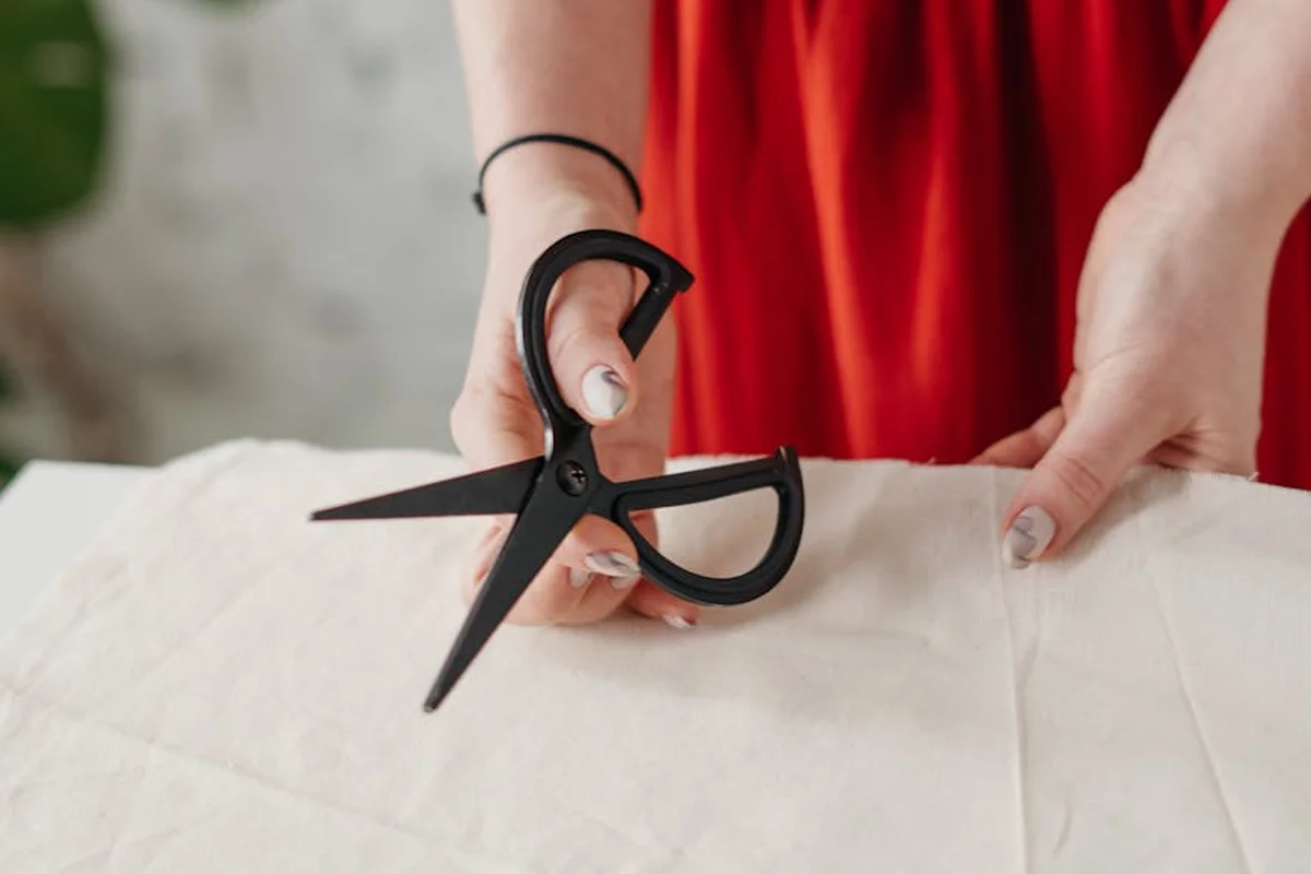 Close-up of hands cutting a light-colored fabric with scissors in a laundry-lab setting.