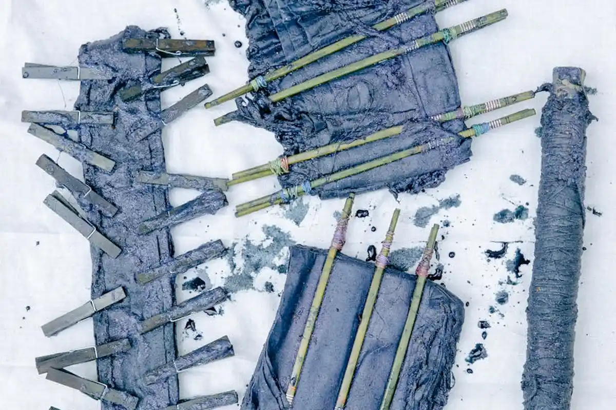Cloth pieces and bamboo skewers stained with blue-purple natural dye, arranged on a work surface, illustrating uneven color and drips during a dyeing experiment.