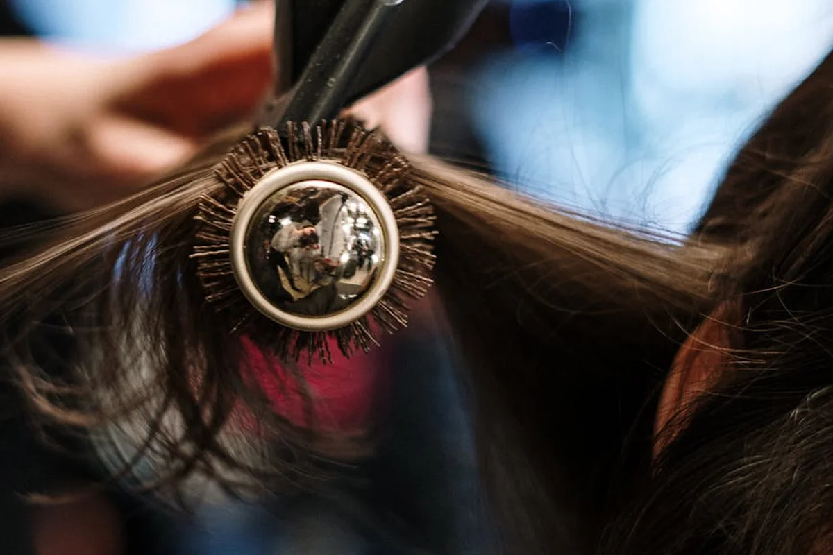 Close-up of a round nylon-bristle hair brush in use on hair, with bristles surrounding a metal barrel.