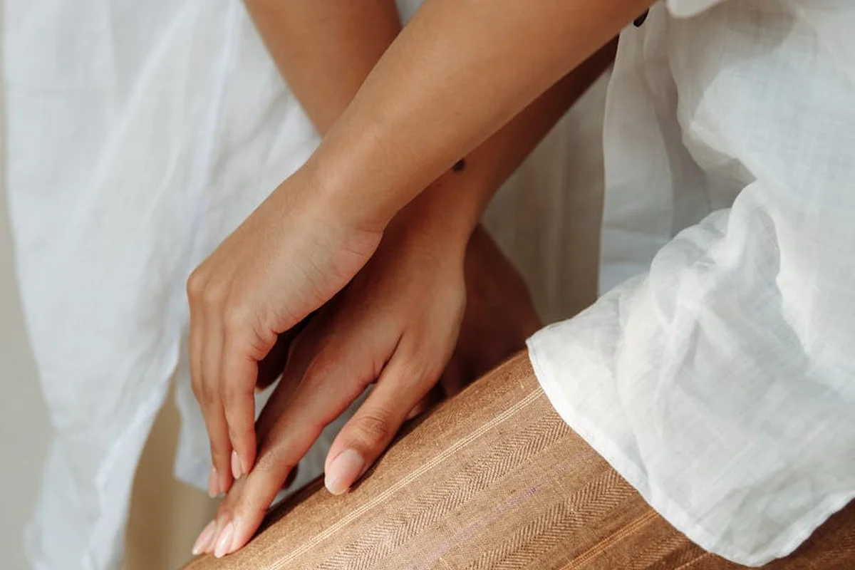 Close-up of hands handling a beige woven fabric or rope with light-colored sleeves in the background
