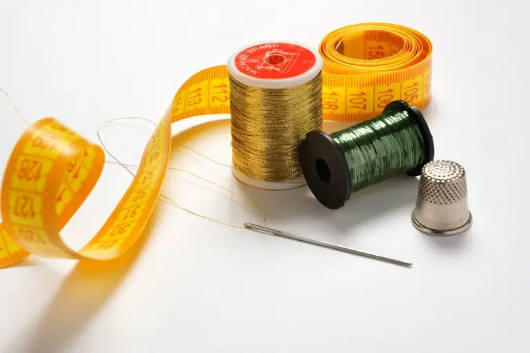 Close-up of sewing tools—measuring tape, spools of thread, needle, and a thimble—on a white surface, suggesting fabric care for nylon flags.