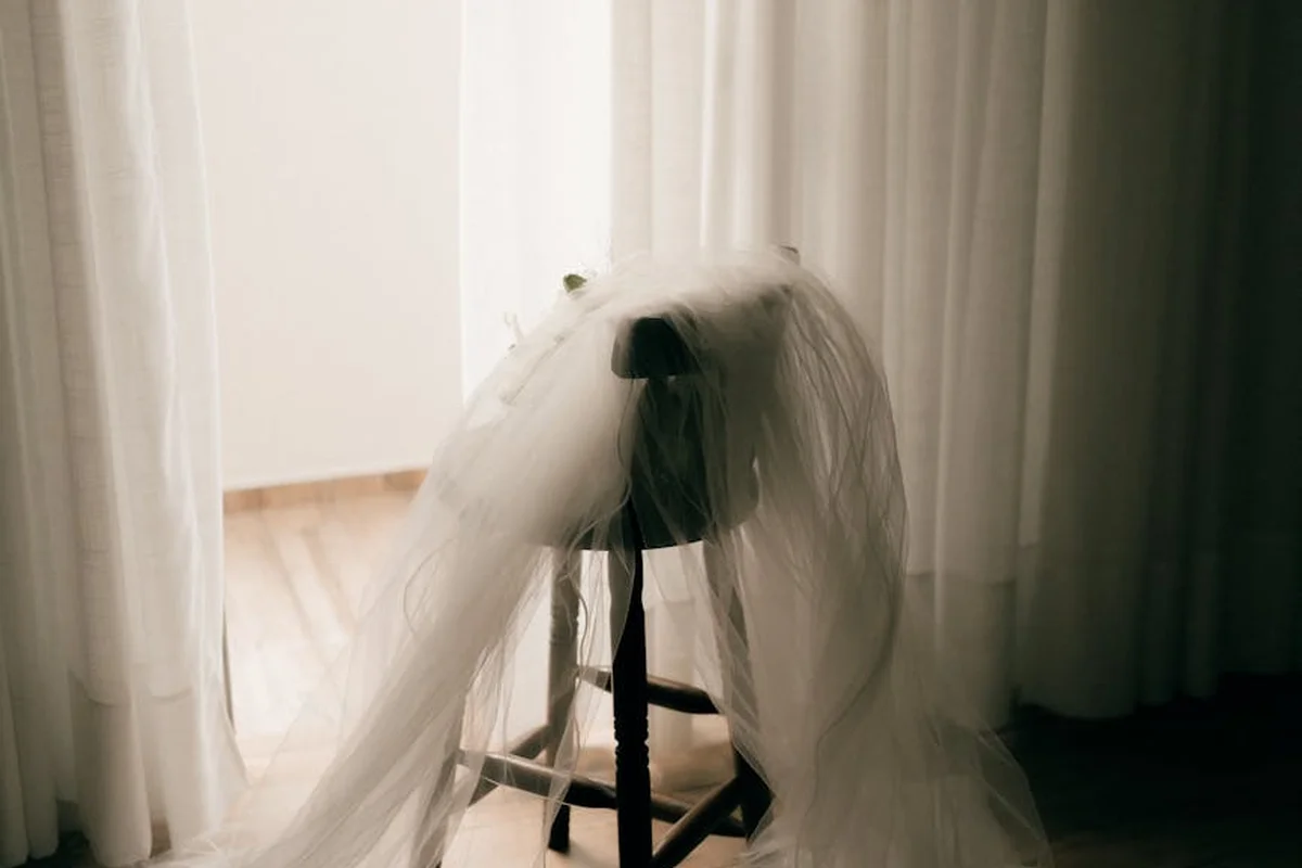 Light-colored fabric draped over a chair in a softly lit room, resembling a sheer veil