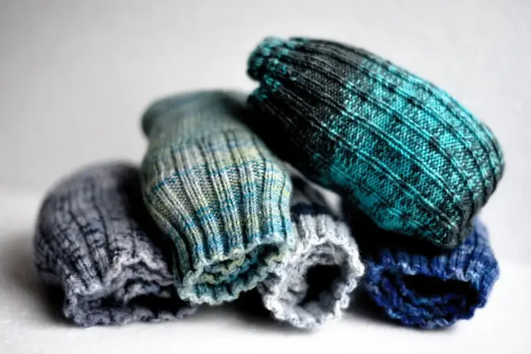 Rolled knitted socks in gray, light gray, teal, and blue tones stacked together