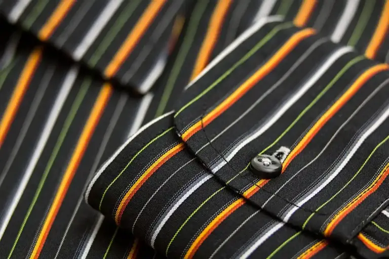 Close-up of striped nylon fabric with black, orange, white, green and yellow stripes and a small button.