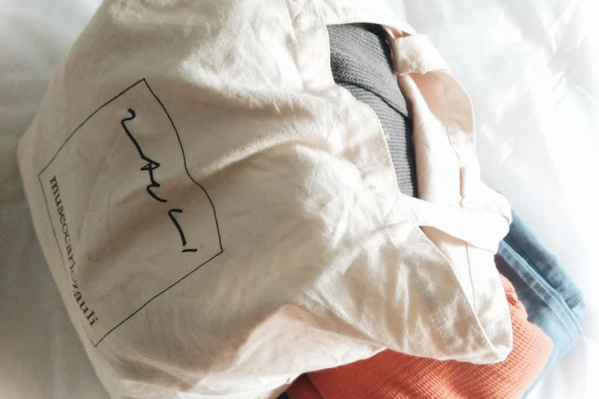 A light pink nylon bag with a brand label lies on a soft surface.