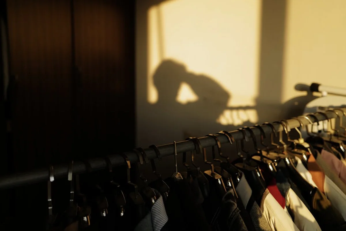 Silhouette of a person casting a shadow on a wall above a row of hanging garments to illustrate focus during fabric bonding.
